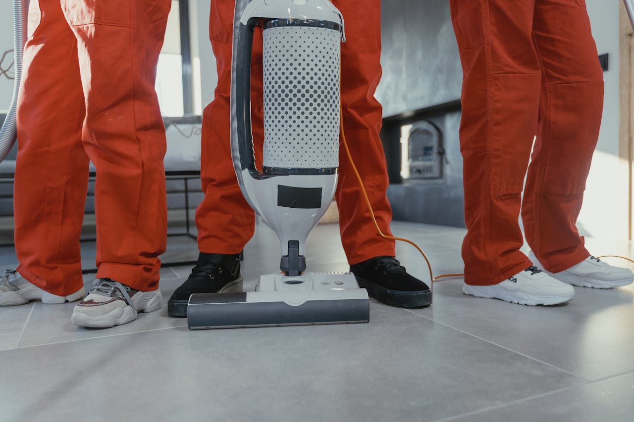 services-04 Team of professional cleaners in red uniforms using a vacuum cleaner indoors.